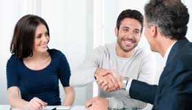 A sales person who got his client to agree and is now shaking hands with him, while the man's wife smiles and looks on.